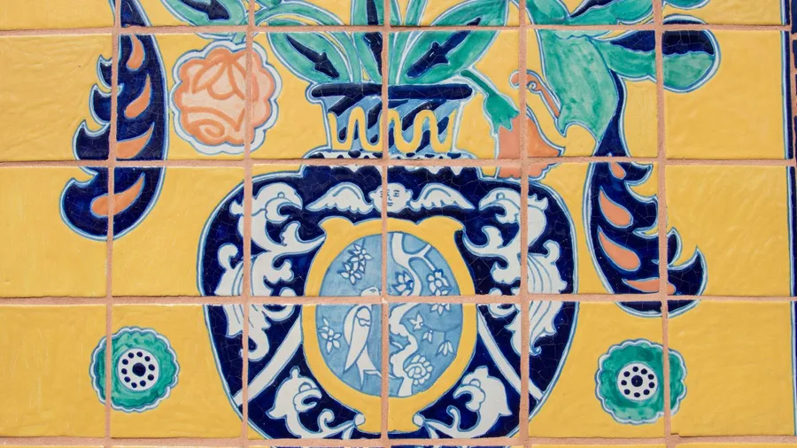 A close-up of colorful Talavera Poblana tiles, featuring a central vase design with elaborate blue and white patterns, surrounded by yellow tiles with orange and green floral motifs.