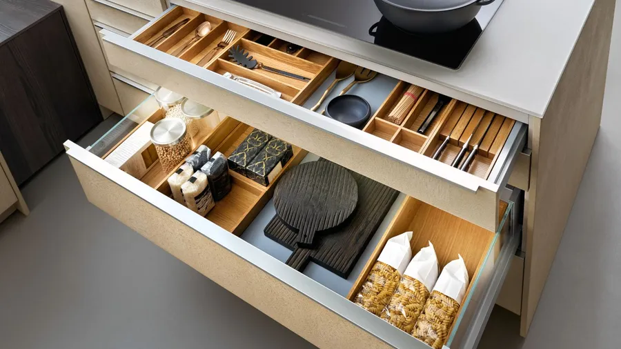A kitchen drawer organized using drawer organizers with utensils, dishes, and pasta.