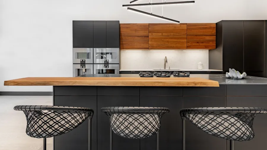A modern contemporary kitchen interior with granite marble countertop with stove, wooden cabinets, sink, statement lights, and bar stools.