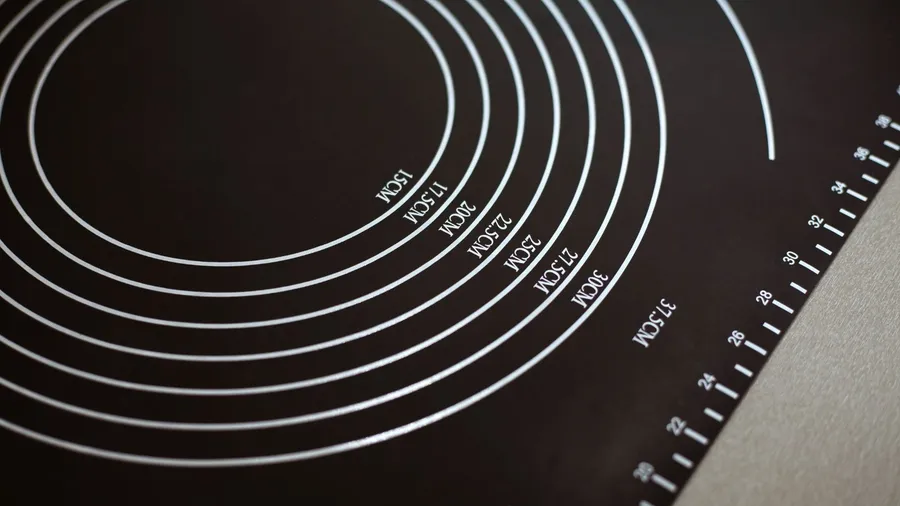 A black silicon baking mat with measurements displayed on it placed on a kitchen table.