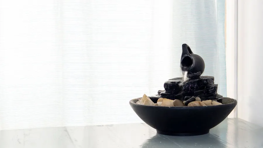 An indoor mini fountain on a white wooden table near a window.