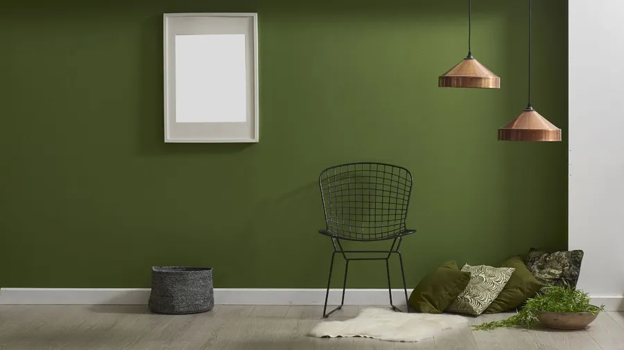 Metal chair, throw pillows, storage basket, plant, rug, metallic light fixture, and poster hanging on an olive green accent wall in a living room.