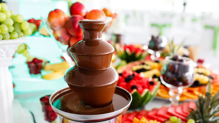 A chocolate fountain with fruits arranged around it.