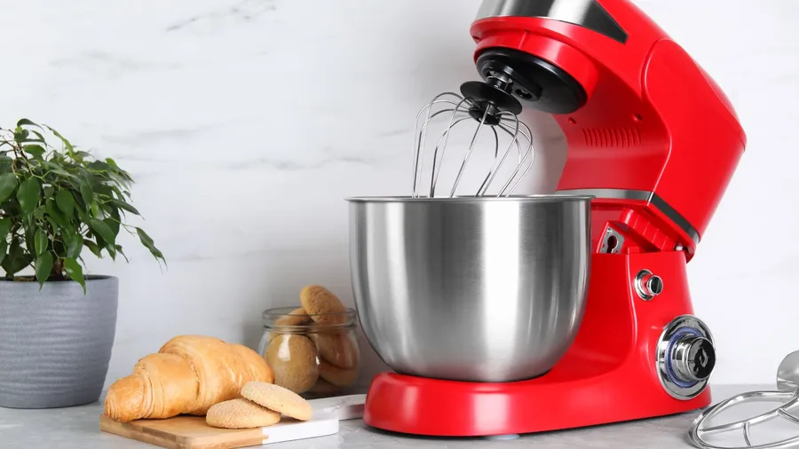 A modern red stand mixer, croissant, and cookies on a light gray marble countertop.