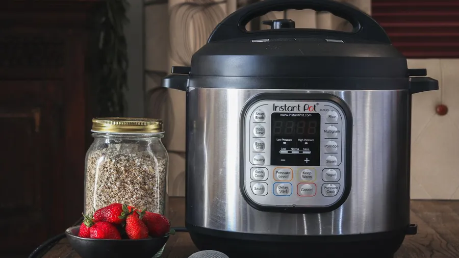 A bowl of strawberries, oats jar, and an instant pot on a wooden table.
