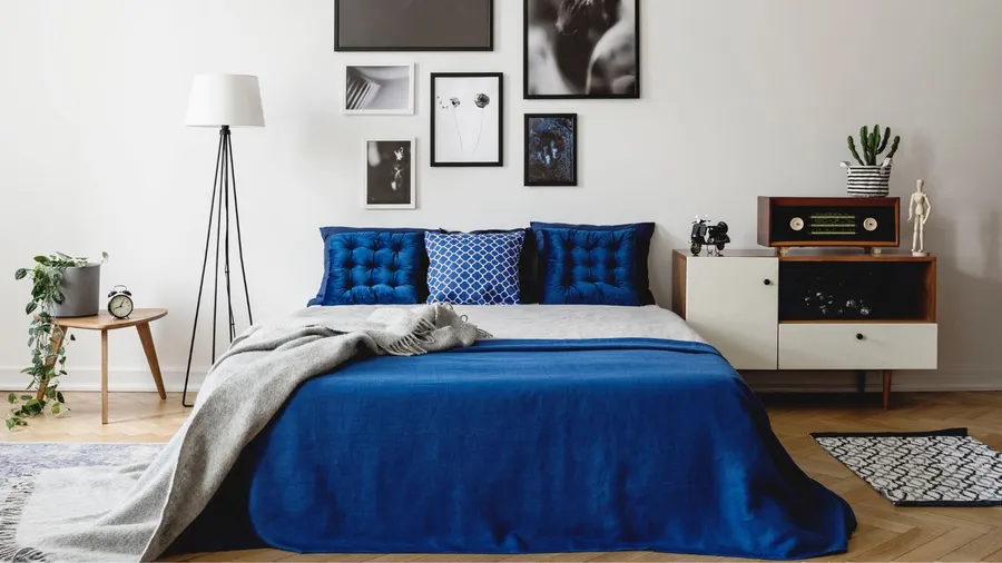A modern bedroom with blue bedding, framed wall art, and a multifunctional nightstand with drawer and a cabinet.