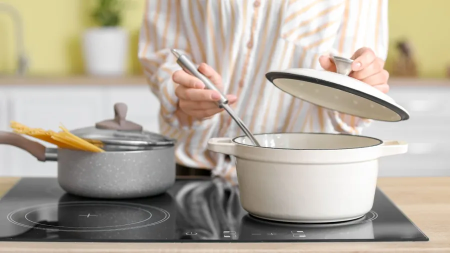 A woman cooking food in a pan on an induction cooktop.