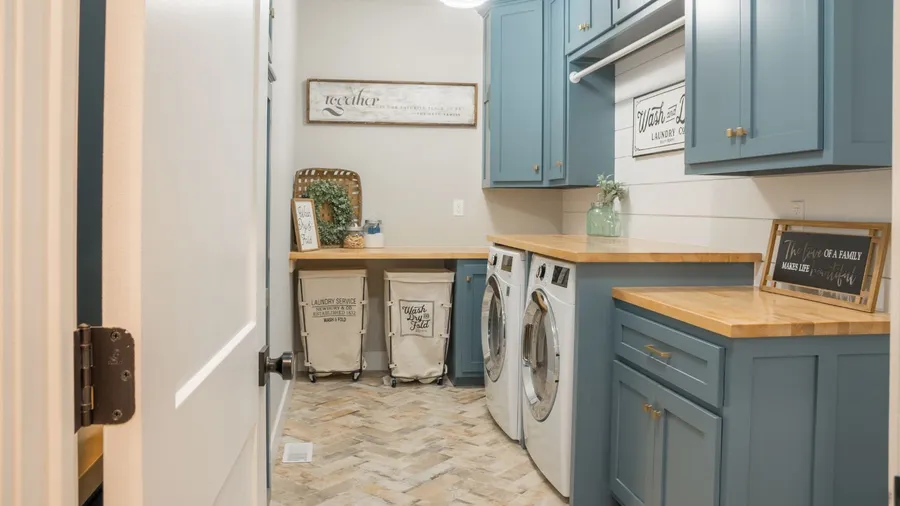 A laundry room interior with blue cabinets, wooden countertops, and rolling hampers for easy sorting.