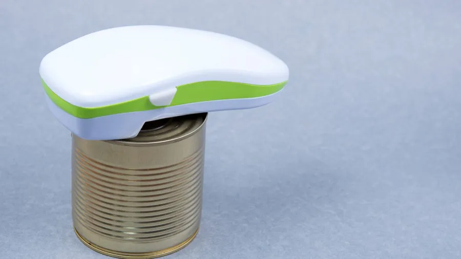 An electric can opener and canned good placed on gray background.