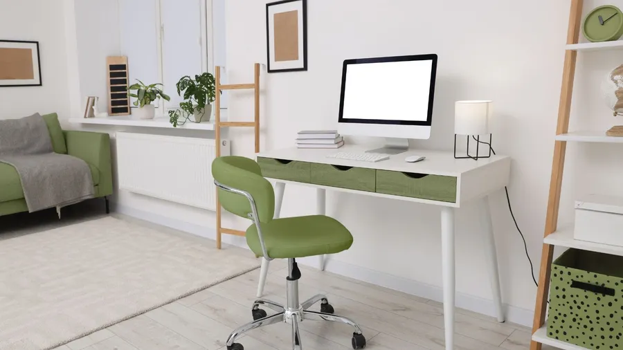 A home office with a computer on white table with drawers and a swivel chair.