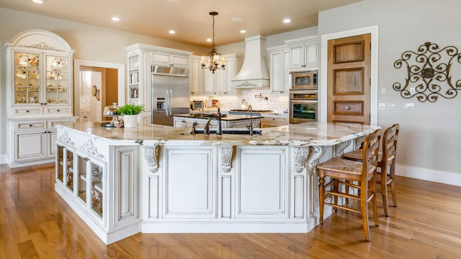 Vintage-style kitchen with ornate white cabinetry, marble island, chandelier, and warm glossy wooden floors adding rich contrast.