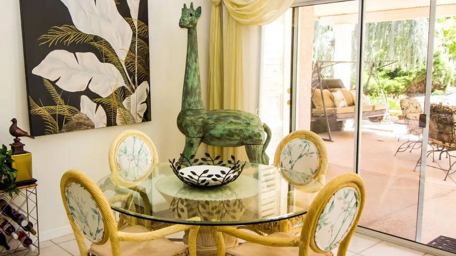 A dining area featuring a glass table, decorative giraffe sculpture, and tropical artwork.