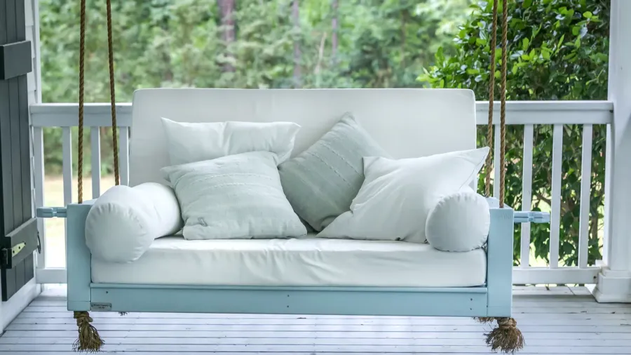 A cozy porch swing in seafoam color with throw pillows.