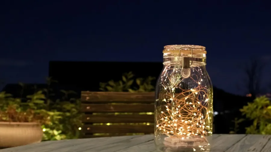 A mason jar with fairy lights in it on a wooden table.