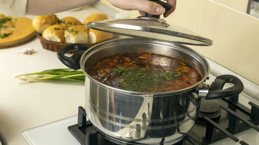 a woman cook opens the lid of a pot of