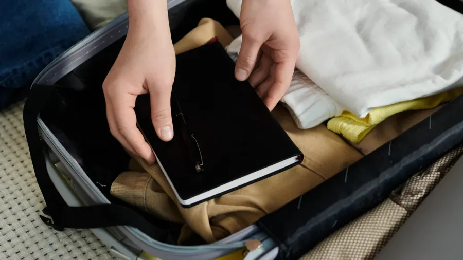 a young woman carefully places a book inside a suitcase