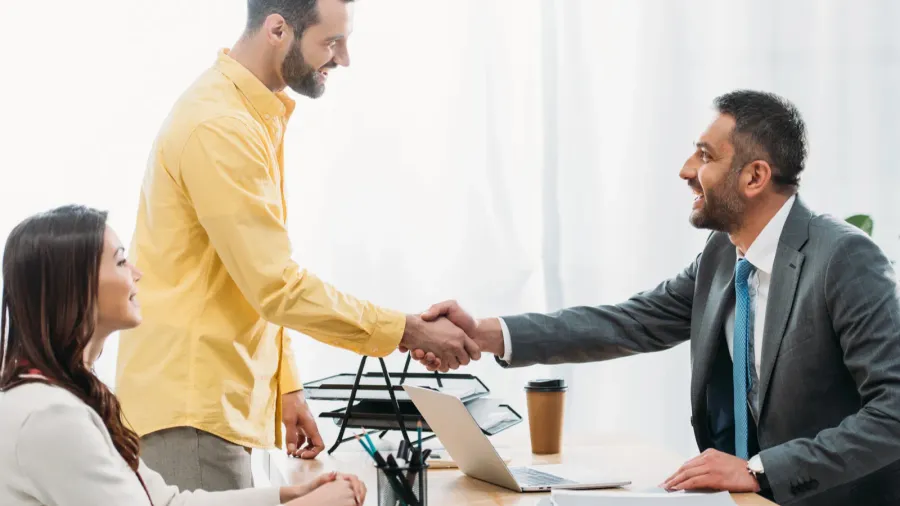 A man in a yellow shirt happily shaking hand with a designer.