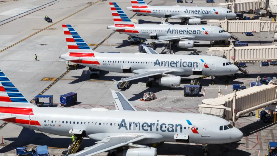 American Airlines planes lined at busy airport gates, jet bridges connected, ground vehicles and personnel coordinating operations.