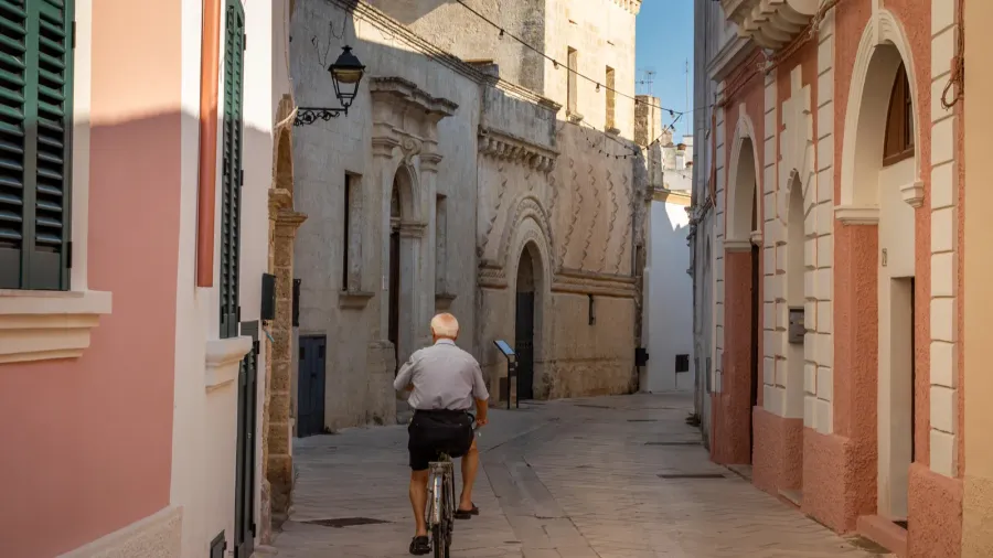 an elderly man with white hair rides a bicycle past