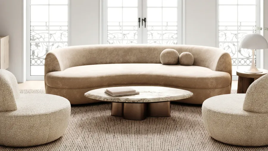 A wellness room with cozy curved sofas, marble top coffee table, rug, and lamp on a wooden side table, illuminated by natural light coming through windows.