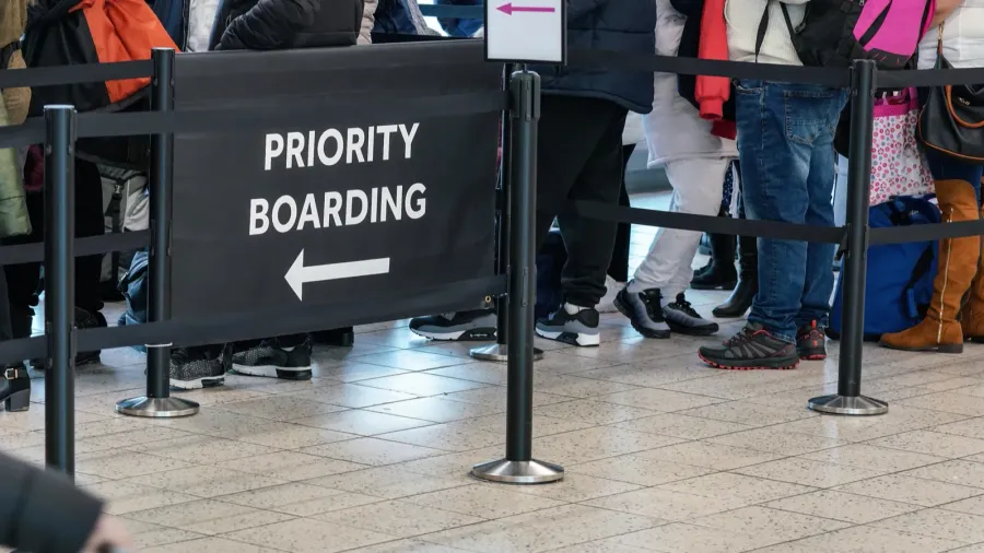 anonymous passengers in queue behind priority boarding sign at the