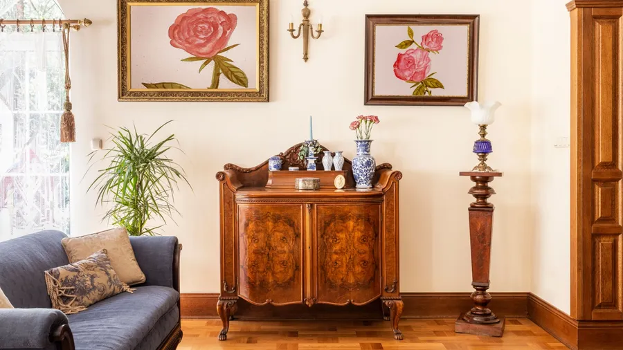 A charming living room setup with a vintage wooden cabinet, decorative vases, and artwork depicting roses against a soft-colored wall.