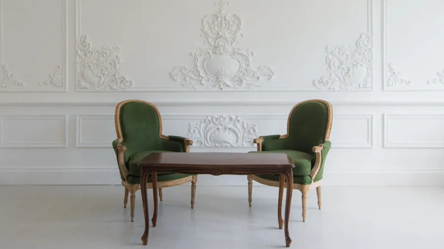 A refined seating area with two green upholstered chairs and a wooden table, set against a beautifully textured wall.
