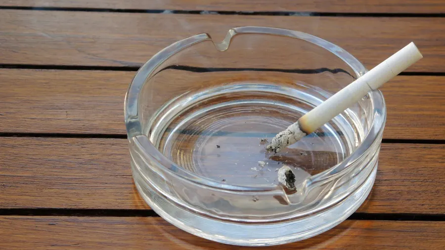 An ashtray containing a cigarette and ash, placed on a wooden table.