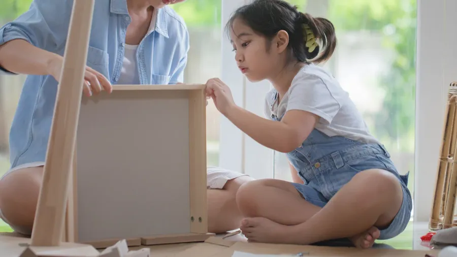 A parent and child working together to assemble a wooden frame or piece of furniture.