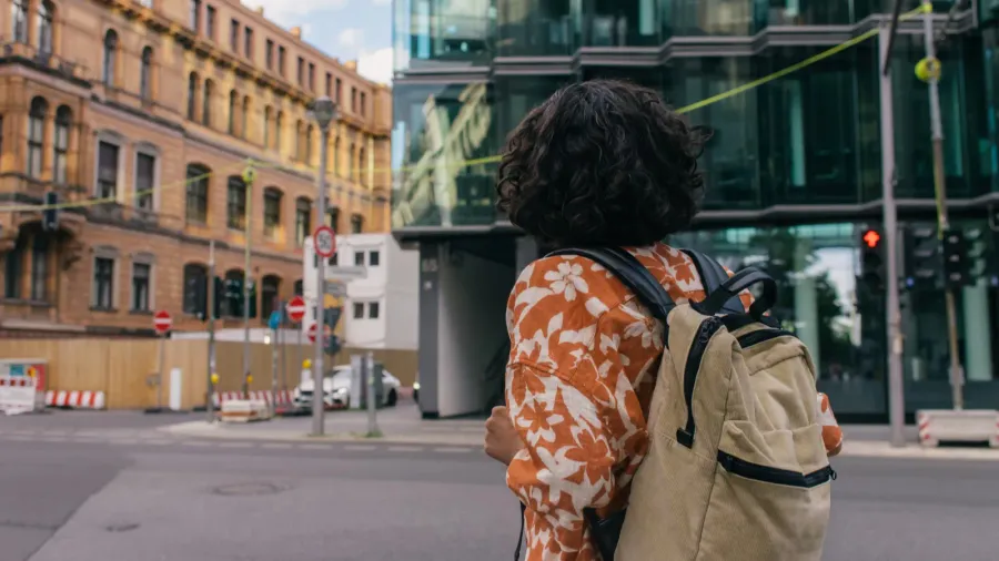 back view of curly young woman with backpack standing on