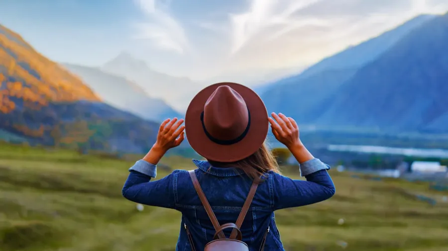 back view of woman traveler wearing hat and backpack traveling