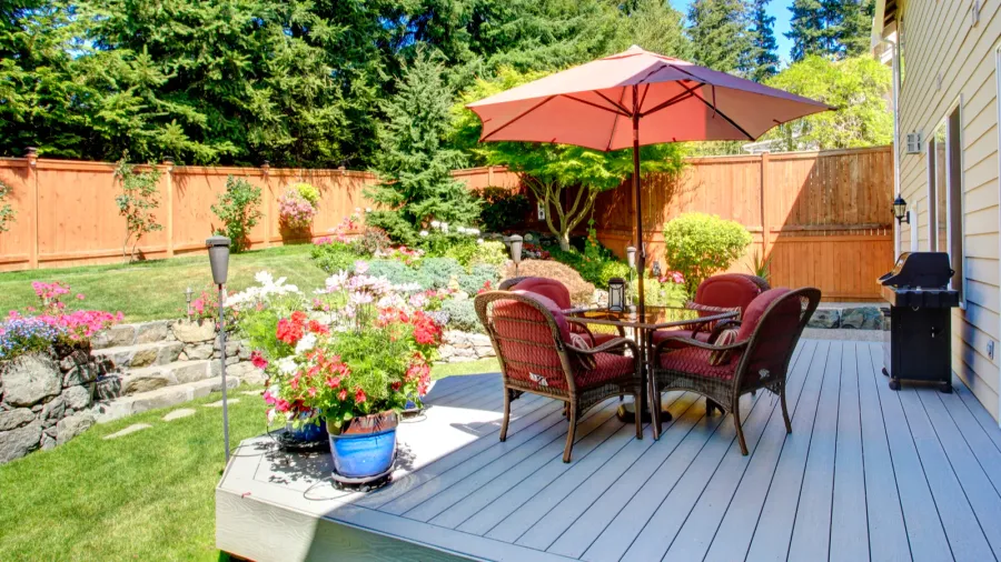 A patio with a dining set on the deck under an umbrella with beautiful landscape.
