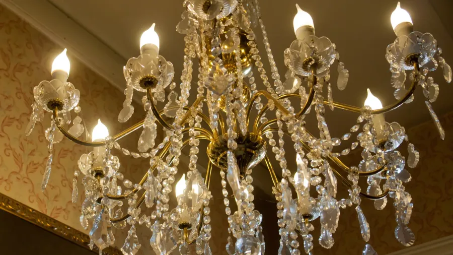 An elegant chandelier with multiple glass and crystal ornaments hanging from a ceiling, emitting warm light.
