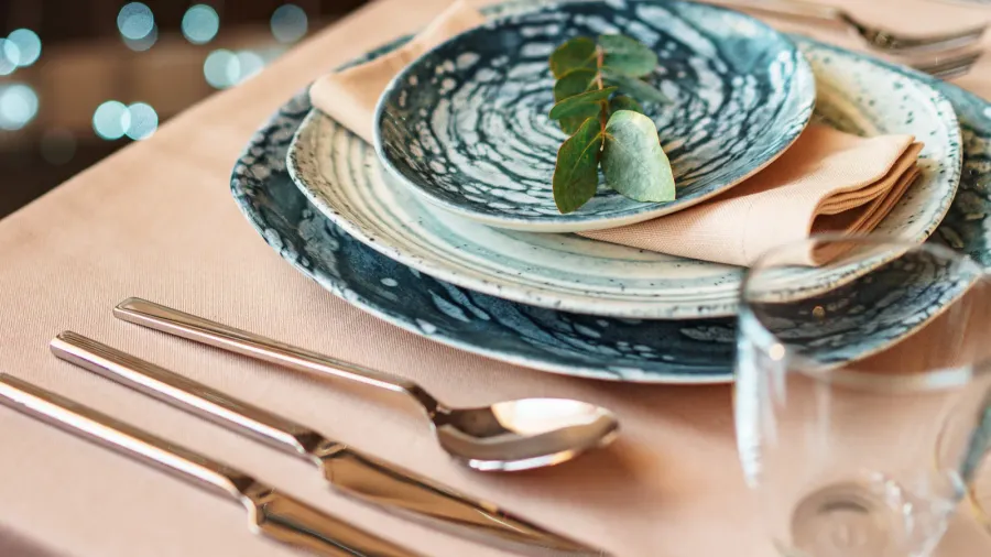 A close-up of elegant dinnerware with blue marbled plates, cutlery, and a beige tablecloth.