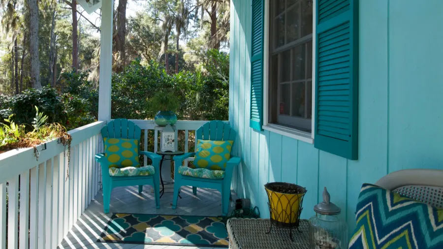 A beautiful porch with chairs with throw pillows, rug, and white wooden railings.