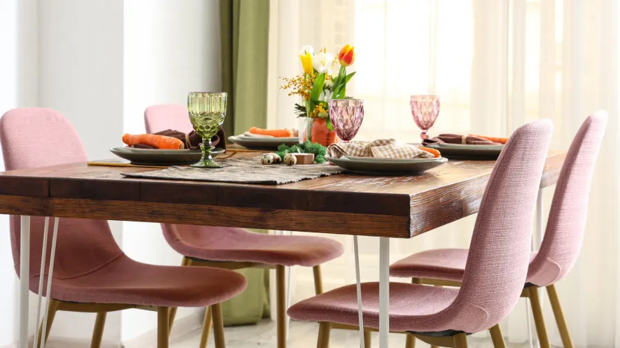A wooden dining table and chairs with beautiful table setting with vibrant flowers in a vase, colorful glassware, and dinnerware.