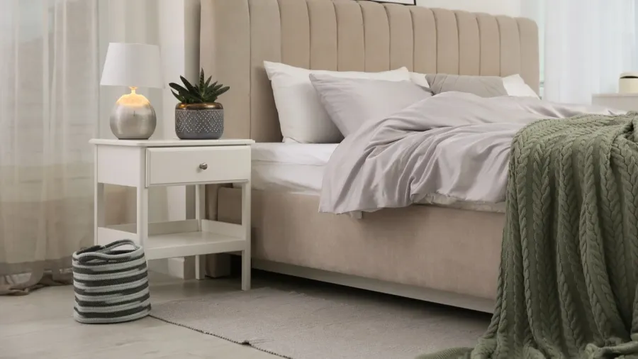 bed with stylish grey linens near white wall in room