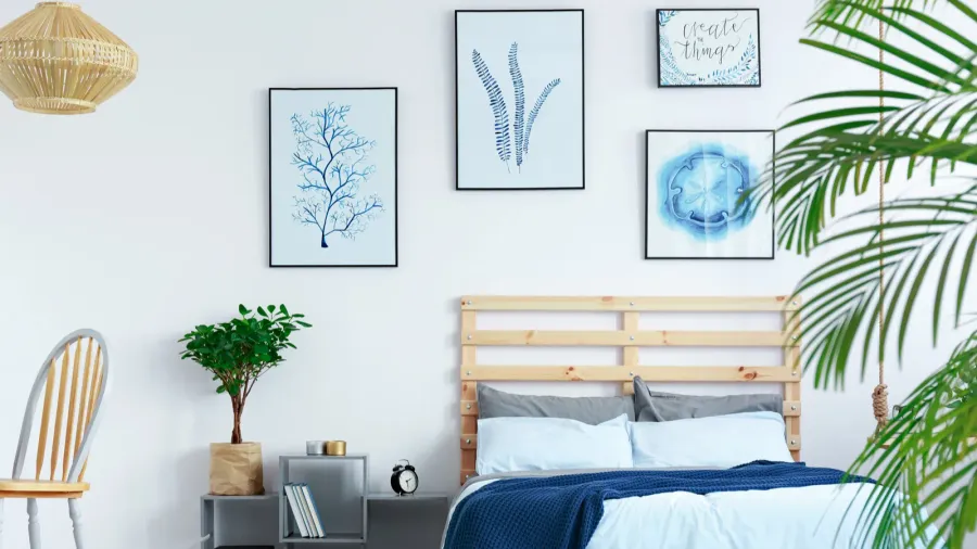 A bedroom interior with pallet wood bed, plants, and framed artwork on the wall.