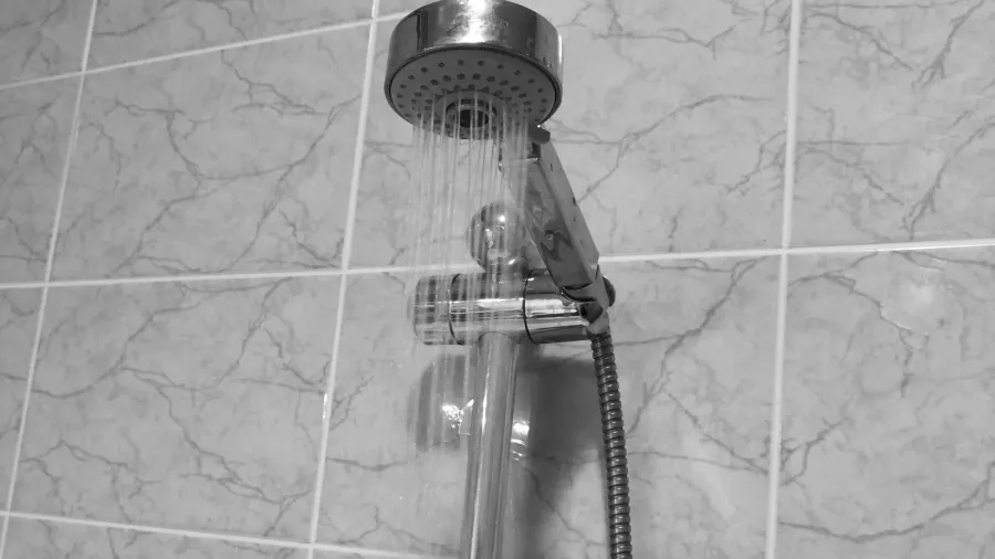 A low-flow chrome showerhead installed on a tiled wall in a bathroom.