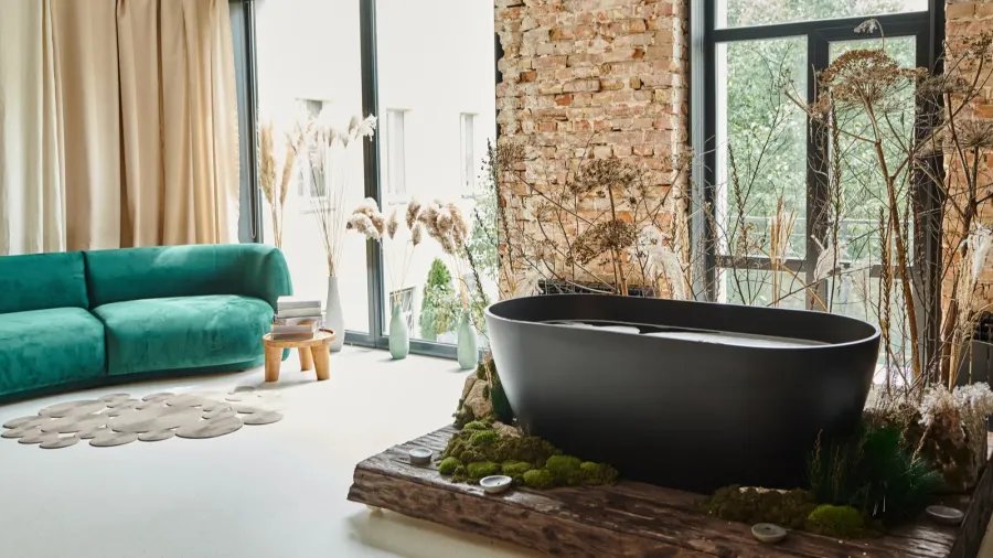 An industrial-style bathroom with a black tub and a cozy green sofa nearby.