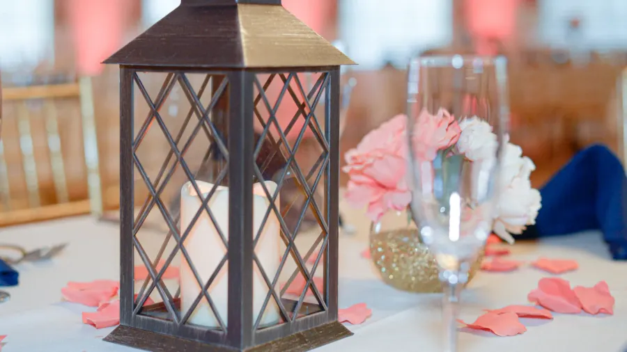 A black lantern with a white candle placed on a white table.