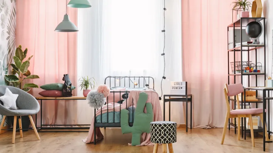 A stylish bedroom interior with a metal bed, throw blanket, armchair, plants, sheer curtains, and decor pieces on the shelf.