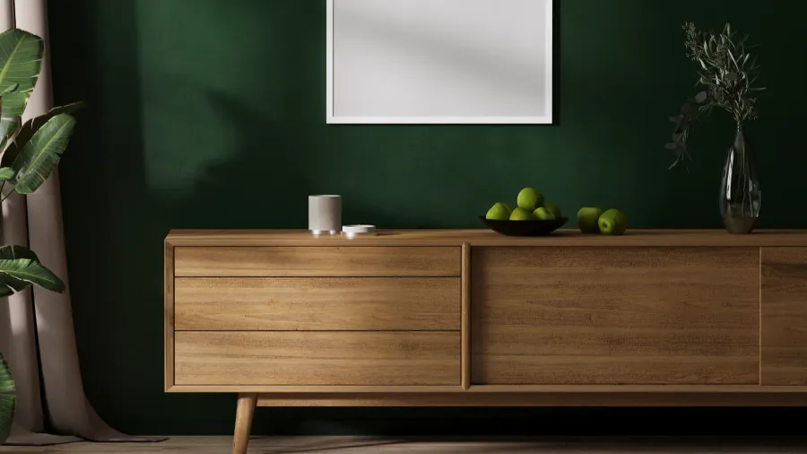 A minimalist living room with a green accent wall, a wooden sideboard, a bowl of green apples, and a potted plant.