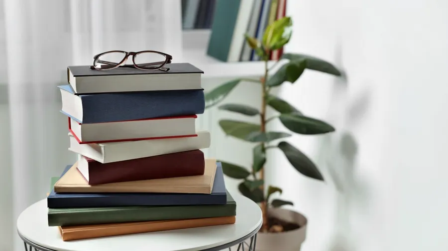 Stack of books and reading glasses on a white table.