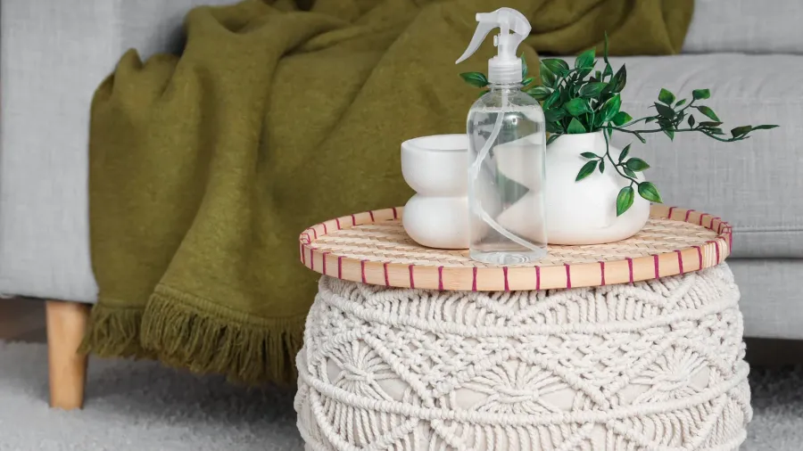 bottle of aroma spray with plant on pouf in living