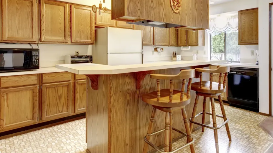 A bright kitchen interior with rustic barstools, wooden cabinets, and wooden island.