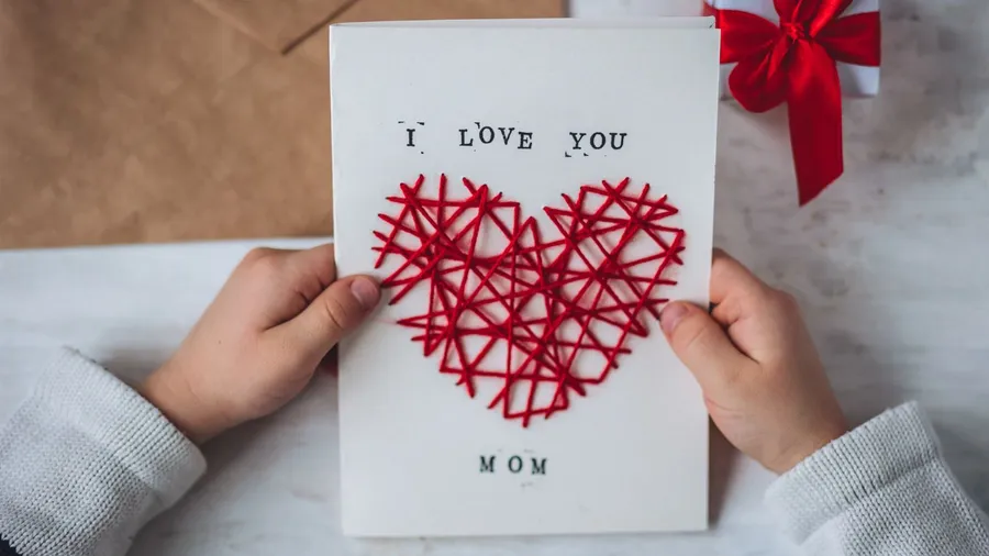 A greeting card reading "I LOVE YOU MOM" with a red string heart.