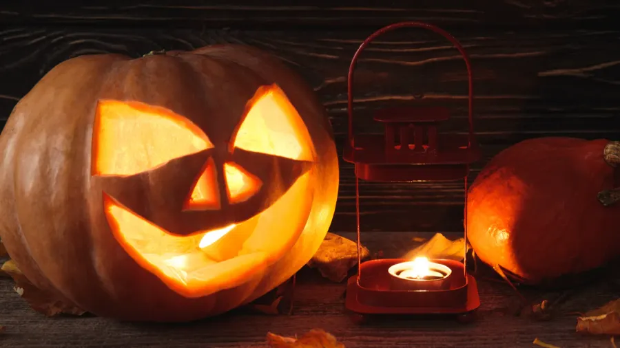 Carved Halloween pumpkin with candle inside. Autumnal leaves and burning candle on wooden rustic table.