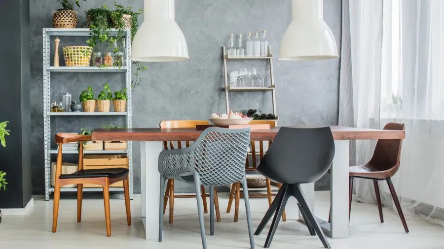 A dining room interior with mix-and-match chairs, wooden table, and potted plants on an industrial style shelf.