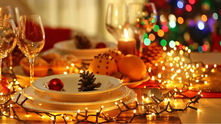 A holiday table setting with dinnerware, glasses, ornaments, and fairy lights.